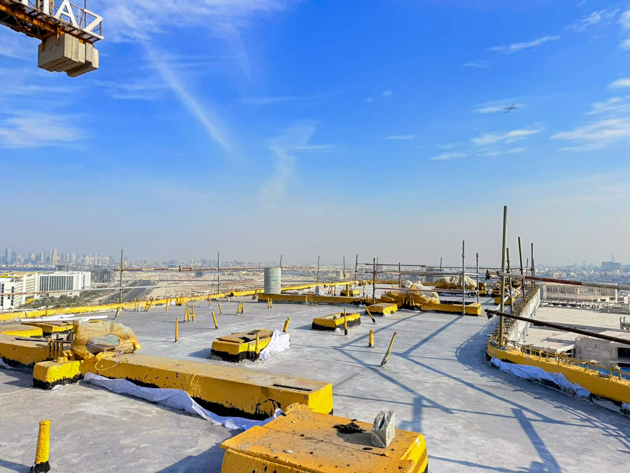 Beach Walk Iii By Imtiaz Construction site rooftop view with yellow barriers, scaffolding, and city skyline under a clear blue sky.